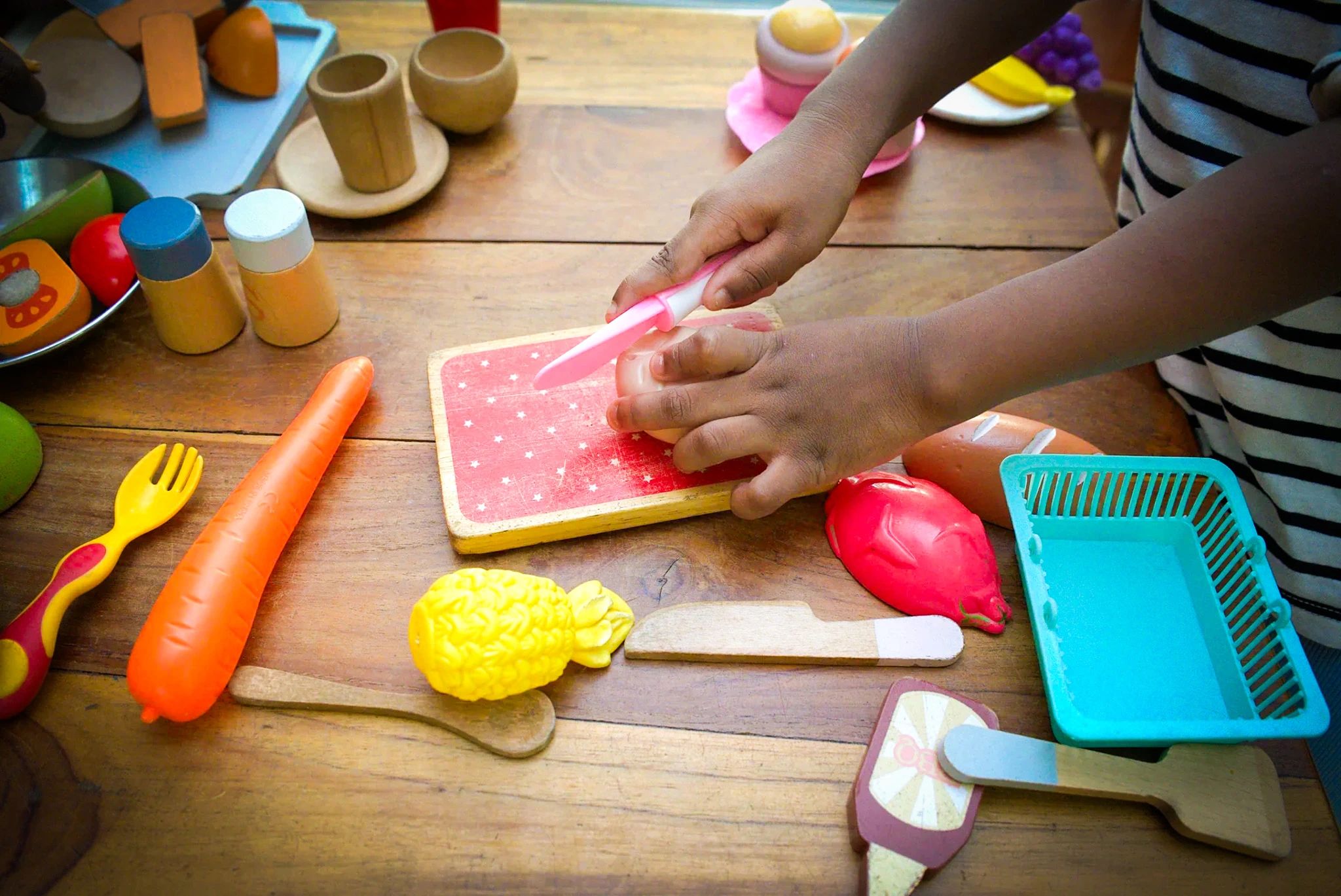 Des mains d’enfant coupent un fruit en bois sur la planche